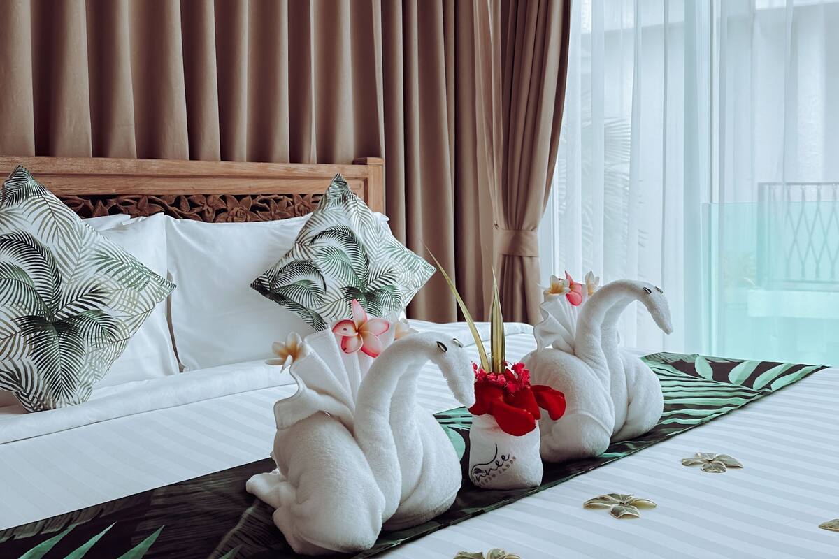 A hotel room with a large bed, brown curtains, a hanging light fixture, and decorative swan pillows.