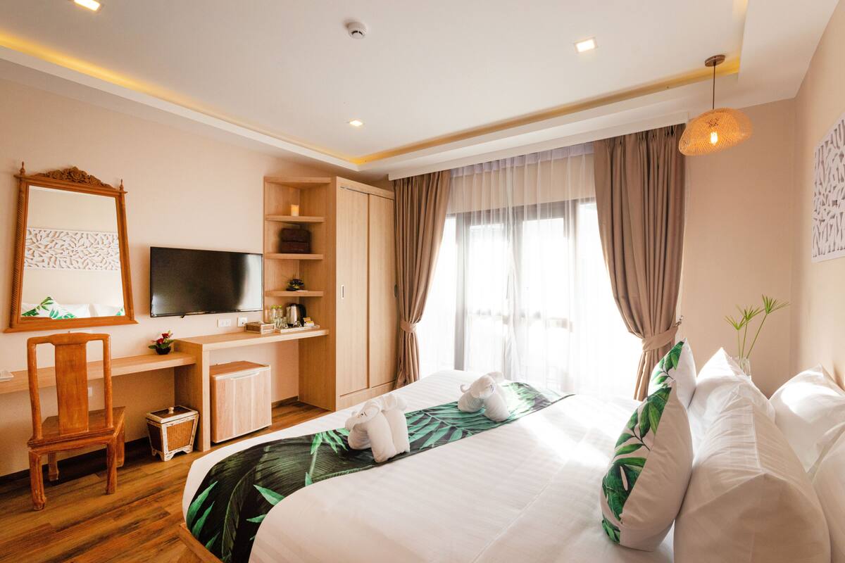 A hotel room with a bed, a desk, a chair, a television, and a window with curtains.