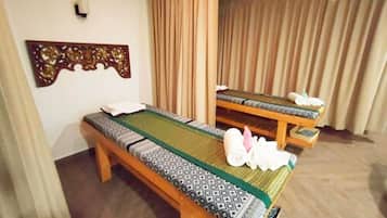 Two massage beds with green mats and patterned blankets are positioned side by side.