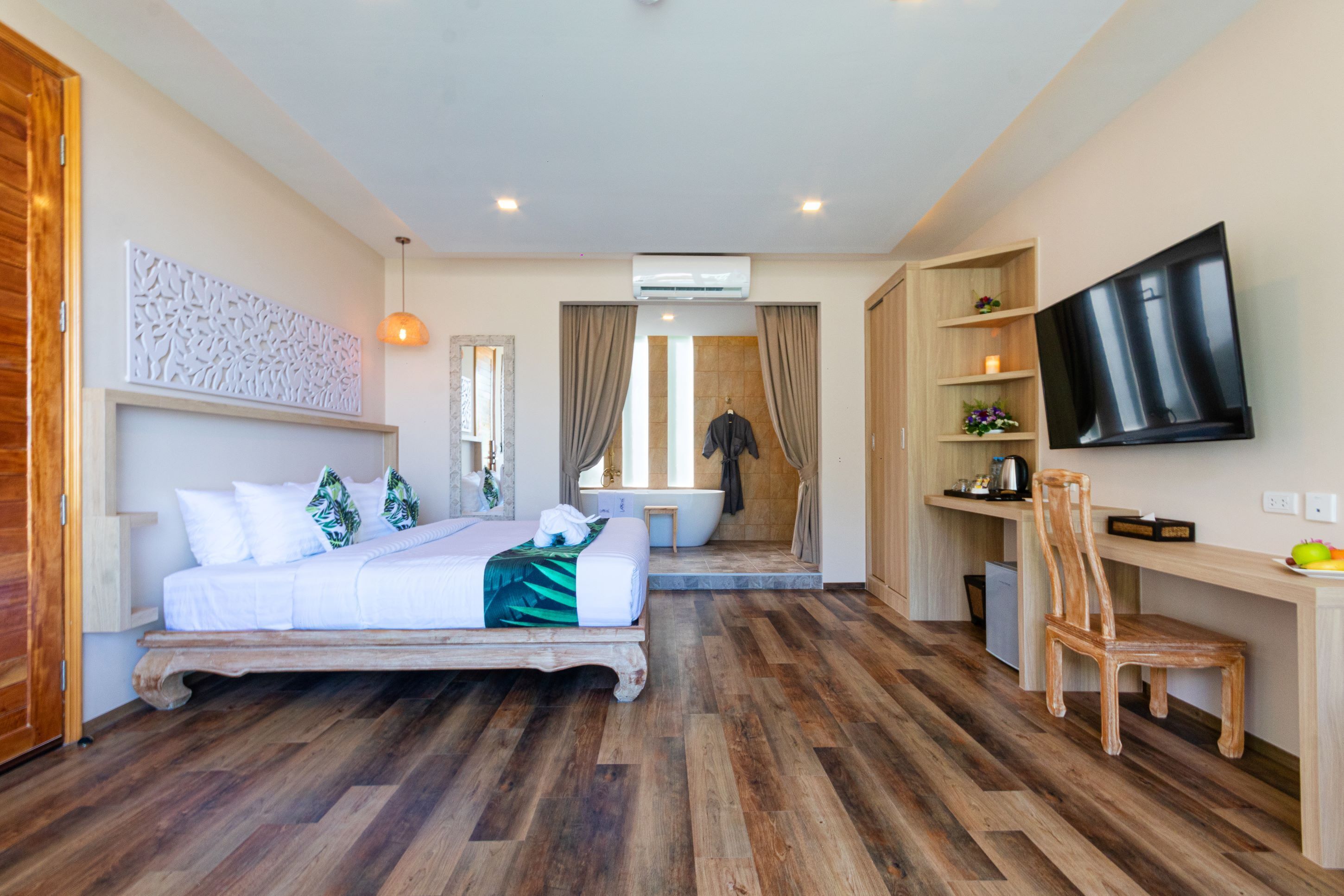 A bedroom with a bed, a desk, a chair, a TV, a bathroom with a bathtub, and an air conditioning unit.