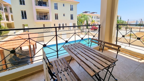 Ein Balkon mit Holztisch und -stühlen mit Blick auf einen Pool und angrenzende Gebäude.