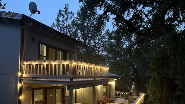 Ein zweistöckiges Haus mit Balkon und Terrasse, mit Lichterketten und Gartenmöbeln.
