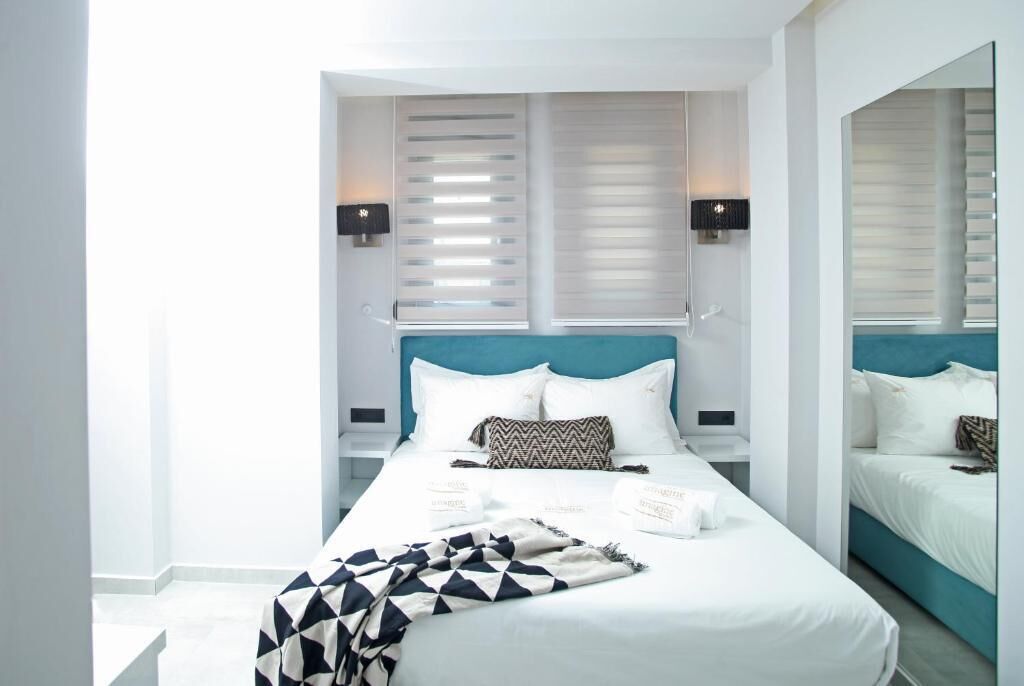 A modern hotel room with a large bed, white bedding, and a teal headboard.