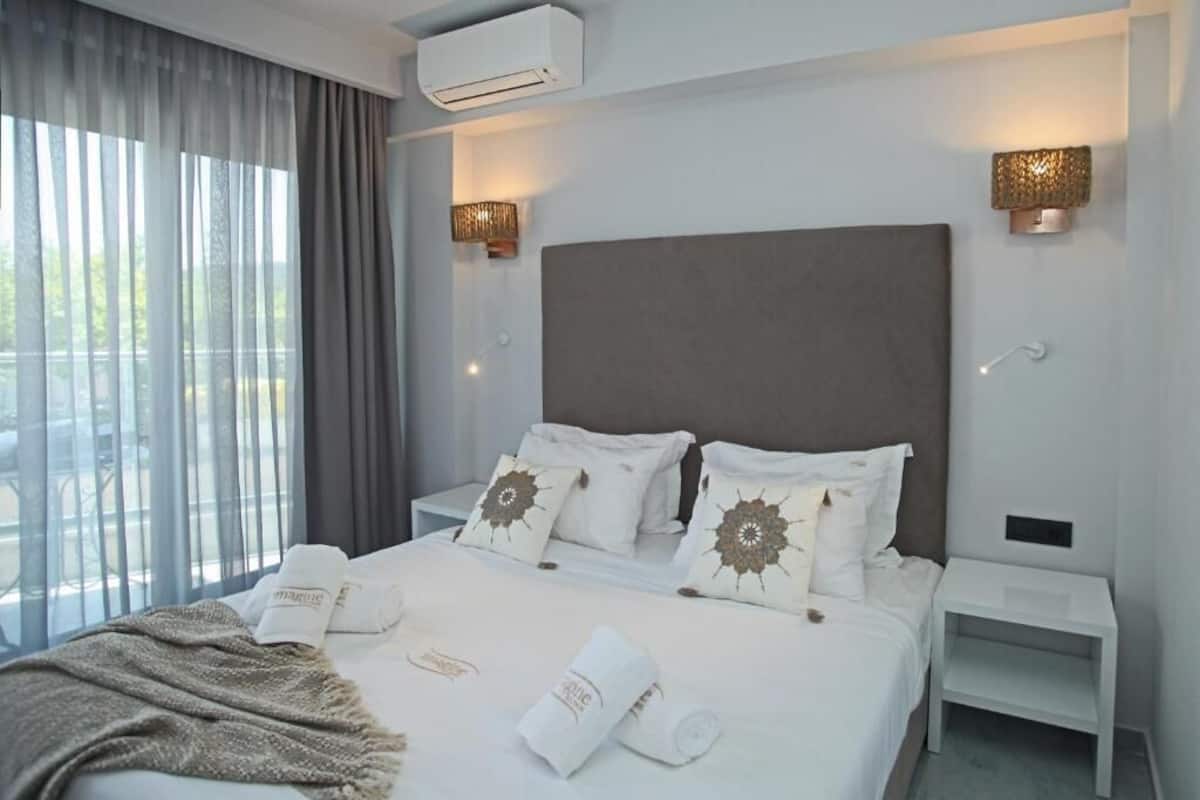 A hotel room with a large bed, two bedside tables, a wall-mounted air conditioner, and two wall sconces.