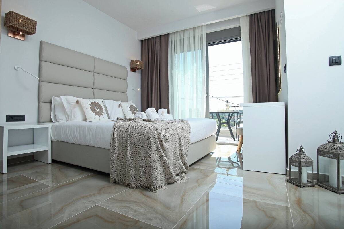 A modern hotel room with a large bed, a small desk, and a balcony with a view.