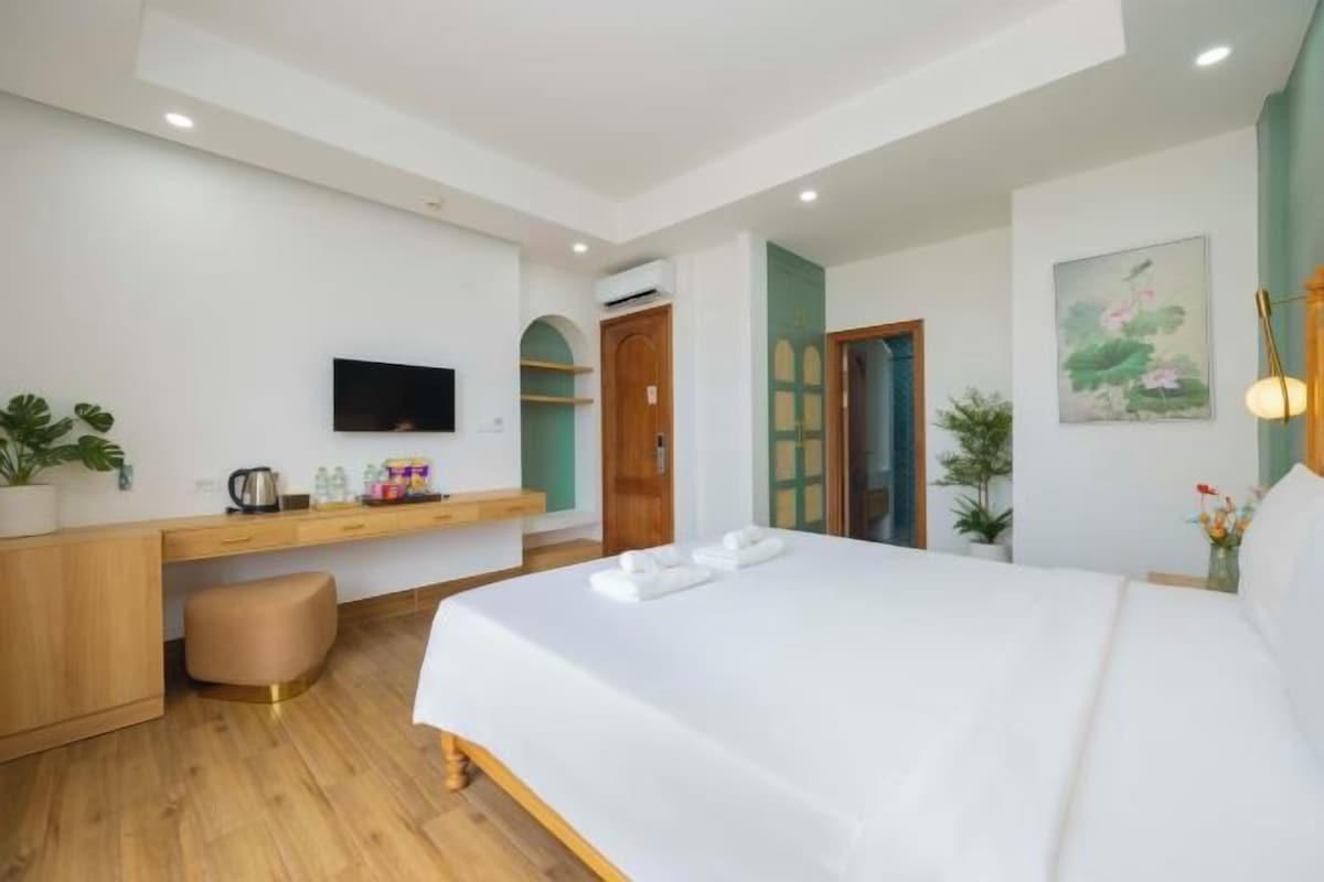 A bedroom with a bed, a desk, a television, and a door.