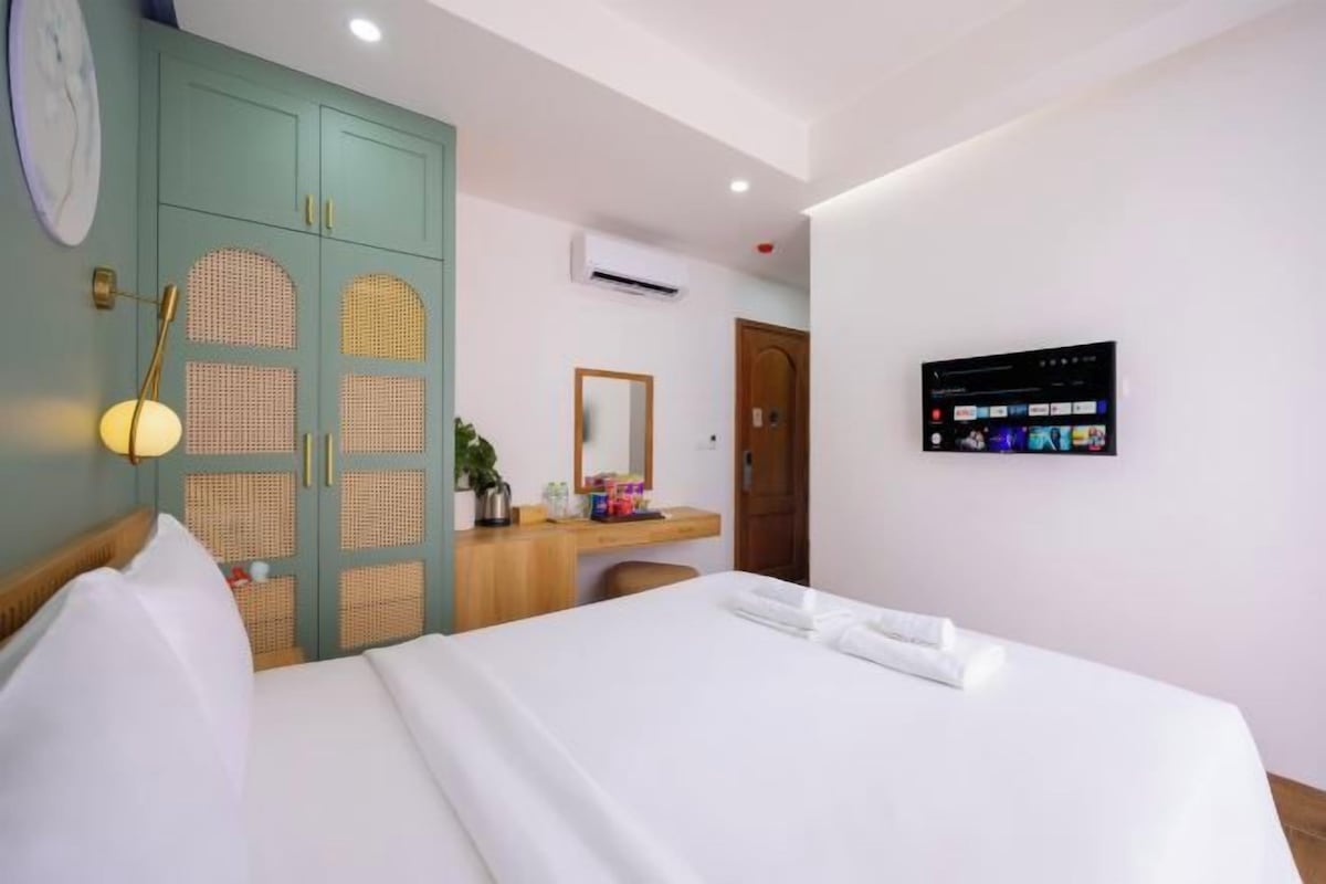 A hotel room with a bed, a desk with a mirror, a wardrobe, and a wall-mounted TV.
