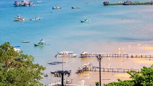 A coastal area with multiple boats docked at a pier, a sandy beach, and a forested area in the background. - Lotus Home Hillside (Phu Quoc)