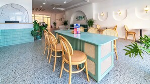 A modern hotel lobby with a central island table, several wicker chairs, potted plants, and a reception desk with a marble accent wall. - Lotus Home Hillside (Phu Quoc)