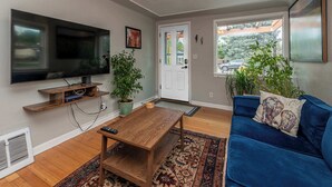 Un salon avec un téléviseur à écran plat, une table basse en bois, un canapé bleu et des plantes en pot.