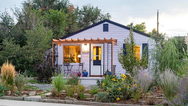 Une maison de plain-pied avec un porche, un petit jardin où poussent des tournesols, et une porte bien visible.