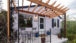 Une véranda couverte avec une pergola en bois, une petite table, deux chaises et des plantes en pot.