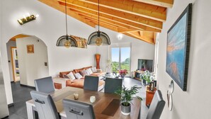 Una sala de estar moderna con techo de madera, una mesa de comedor con sillas, un sofá y un televisor.