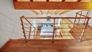 Una escalera de madera con barandilla metálica que lleva a un dormitorio con cama y ventana.