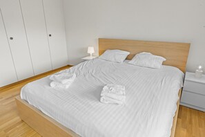 A neatly made bed with white linens, a wooden headboard, and a nightstand with a lamp. - Appartement central et confortable (Crans (VS))
