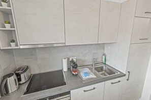 A modern kitchen with a built-in stove, a sink, and a kettle. - Appartement central et confortable (Crans (VS))