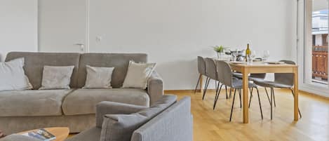 A living room with a sofa, a dining table with chairs, and a wooden floor.