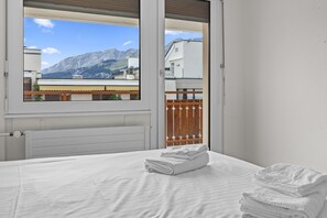A bedroom with a bed, a window with a view of mountains, and a radiator. - Appartement central et confortable (Crans (VS))