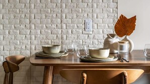 Un coin repas avec un mur en briques, une table en bois mise avec des assiettes, des bols et une sculpture décorative en forme de feuille.