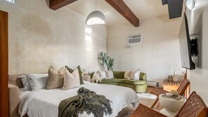 Une chambre à coucher avec un lit, un canapé vert, une chaise en bois et un téléviseur fixé au mur.