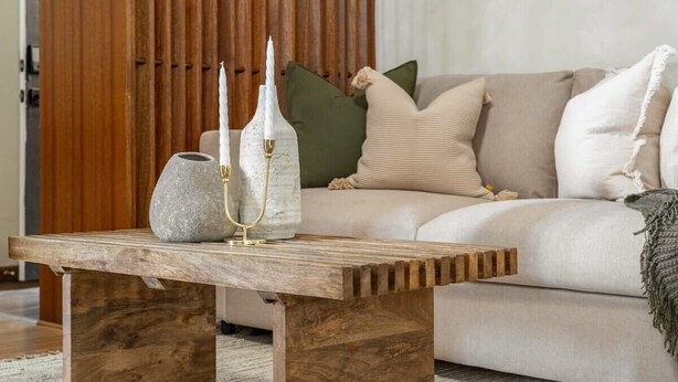 Une table basse en bois, ornée d’un vase et de bougeoirs.