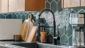 Une cuisine avec un évier noir, une planche à découper en bois, une bouteille et une machine à café.