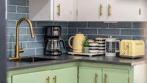A kitchen with a black sink, a coffee maker, a yellow kettle, a toaster, and a blender on the counter. - The Mango  Vibrant Oasis Sleeps 4  Downtown Fun (Drumheller)