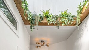 A hallway with a wooden ceiling, black and white walls, a staircase, and a hanging plant arrangement. - The Mango  Vibrant Oasis Sleeps 4  Downtown Fun (Drumheller)