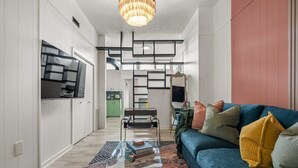 A modern living room with a blue sofa, a glass coffee table, and a patterned rug. - The Mango  Vibrant Oasis Sleeps 4  Downtown Fun (Drumheller)
