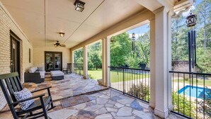 A covered patio with stone flooring, outdoor seating, and a view of a swimming pool. - The Wexford French Chateau w/ Pool (Athens)
