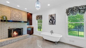 A spacious bathroom with a freestanding bathtub, a fireplace, and large windows offering a view of the outdoors. - The Wexford French Chateau w/ Pool (Athens)