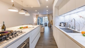A modern kitchen with a central island, stainless steel appliances, pendant lighting, and a view to a balcony. - Modern Beautiful Pool And Sea Apt Qawra (St. Paul's Bay)