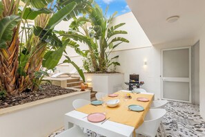 Un coin repas avec une table dressée pour quatre personnes, entourée de chaises blanches, d’une table en bois et d’une variété d’articles de vaisselle.