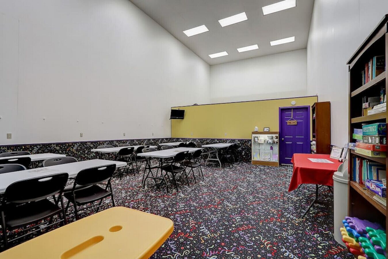 Une salle de classe avec des bureaux, des chaises, une bibliothèque et une porte.