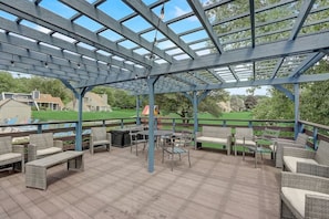 Un patio couvert aménagé avec du mobilier d’extérieur, une pergola dotée d’un toit en verre et une vue sur un terrain de golf en arrière-plan.
