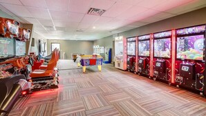 A room with a pool table, arcade games, and a racing simulator.