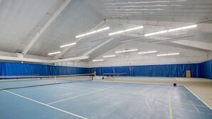 An indoor tennis court with a net, blue flooring, and overhead lighting.
