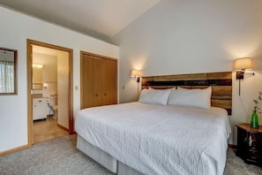 Une chambre à coucher avec un grand lit, une tête de lit en bois, deux lampes de chevet et une petite table de chevet sur laquelle est posé un vase.