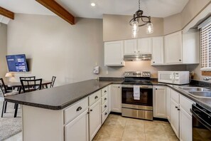A kitchen with white cabinets, a granite countertop, stainless steel appliances, and a dining area with chairs. - Grace-Jo @ Tamarack Highland 5 (Wisconsin Dells)