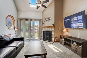 A living room with a fireplace, a sofa, a coffee table, a TV displaying streaming services, and a ceiling fan. - Grace-Jo @ Tamarack Highland 5 (Wisconsin Dells)