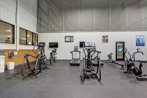 Ein Fitnessraum mit unterschiedlichen Trainingsgeräten, einem Fernseher und einer Tür.