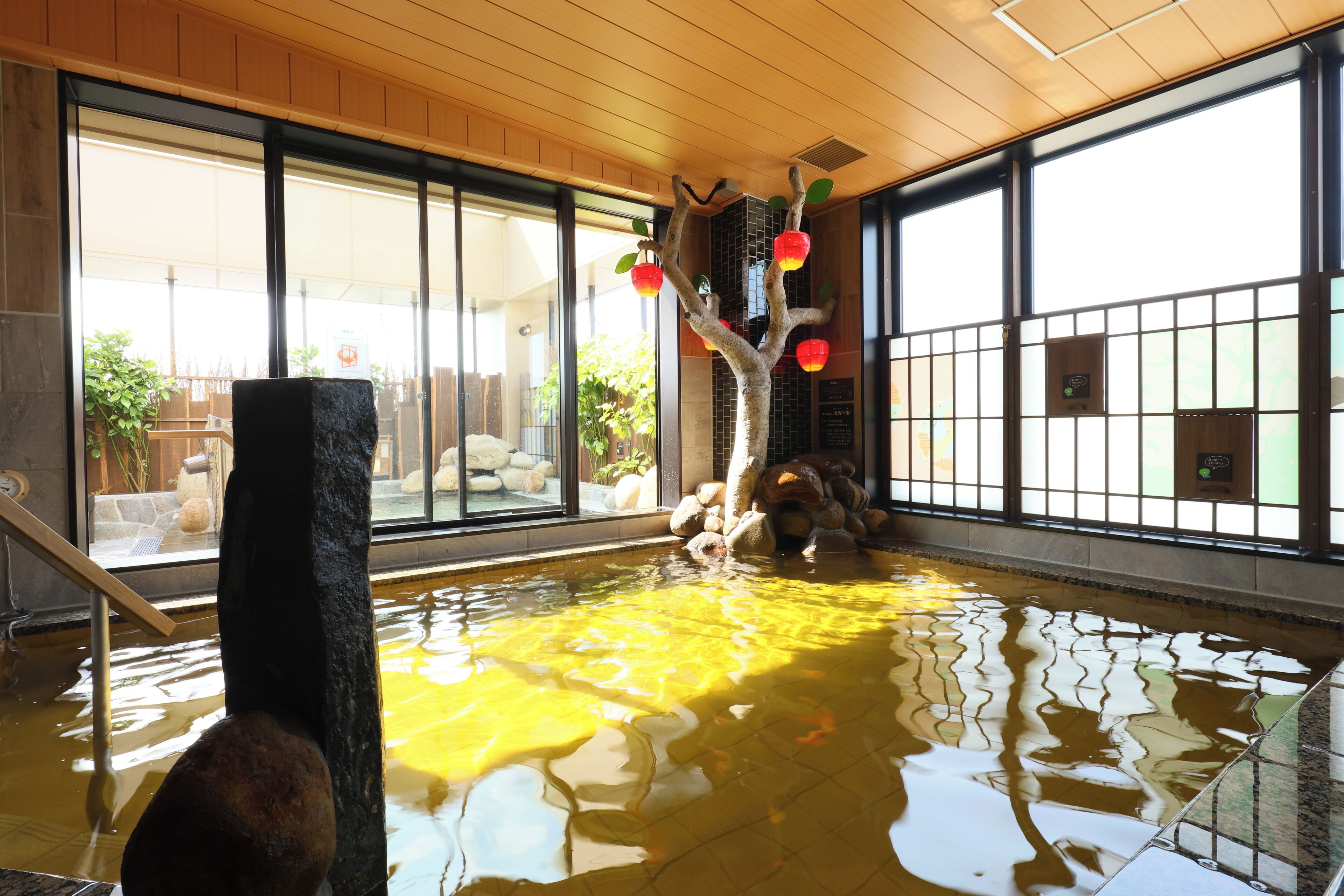 A room with a large window, a wooden ceiling, and a water feature with a tree and red lanterns.