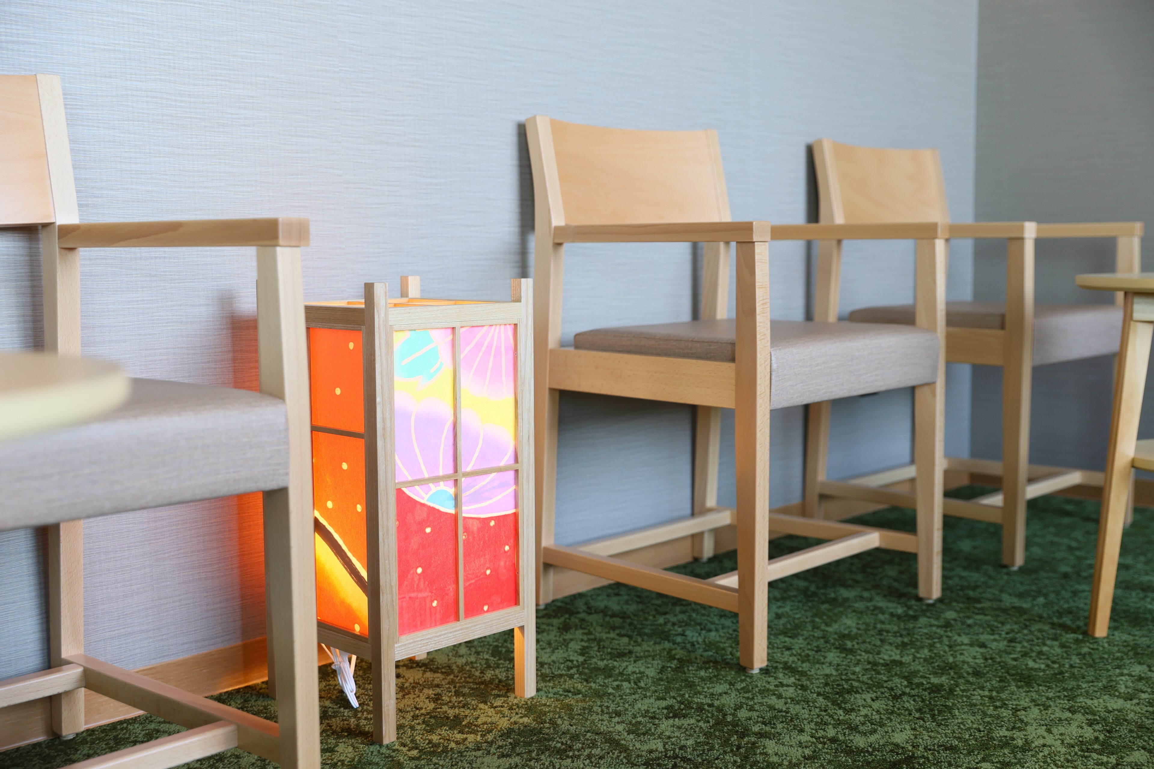 A row of wooden chairs with cushioned seats and backs, arranged against a wall with a green carpeted floor.