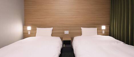 A hotel room with two single beds, a wooden headboard, bedside lamps, and a green curtain.