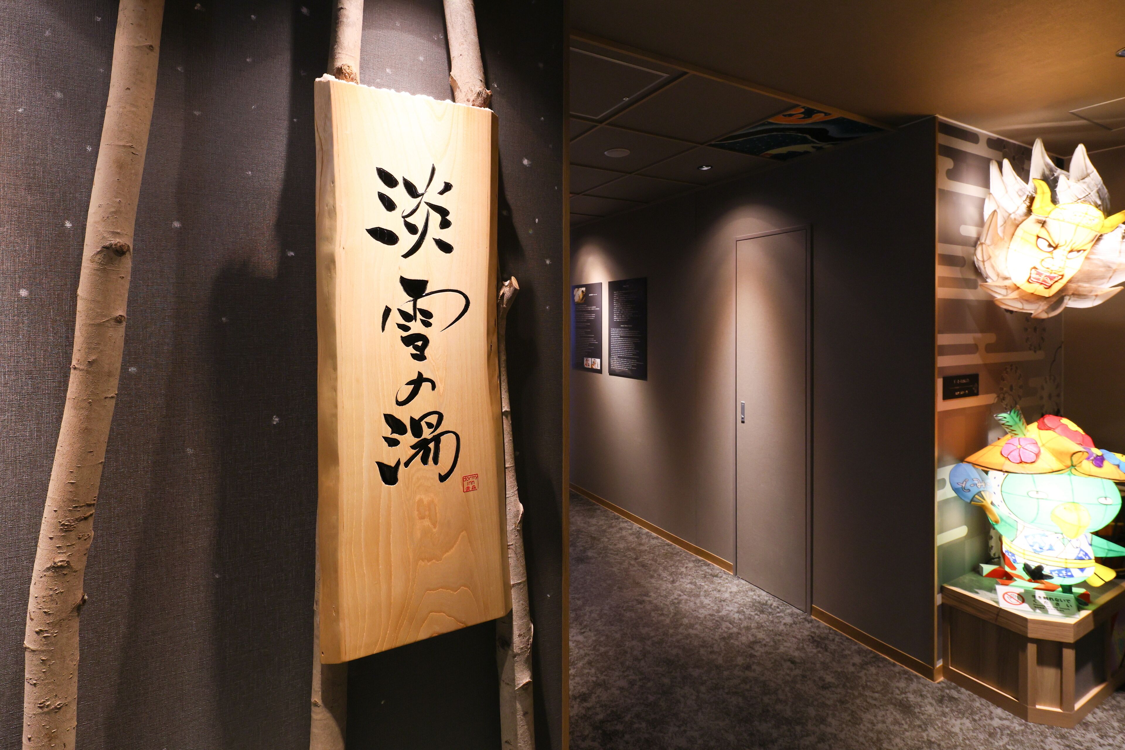 Un pasillo con un letrero de madera con caracteres japoneses, una puerta y un adorno decorativo y colorido sobre una mesa.