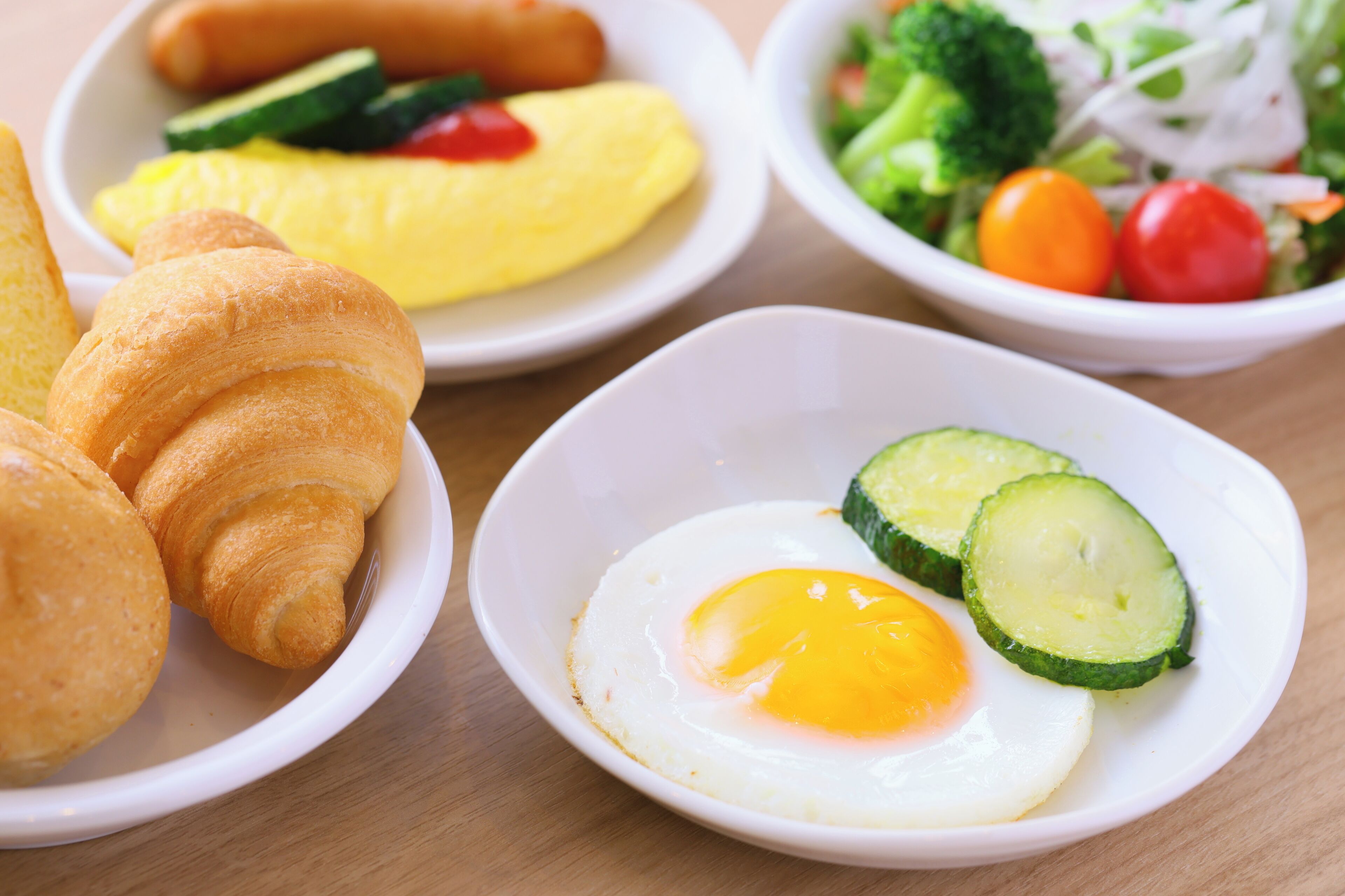 Un desayuno con croissants, una tortilla, un huevo frito y una ensalada.