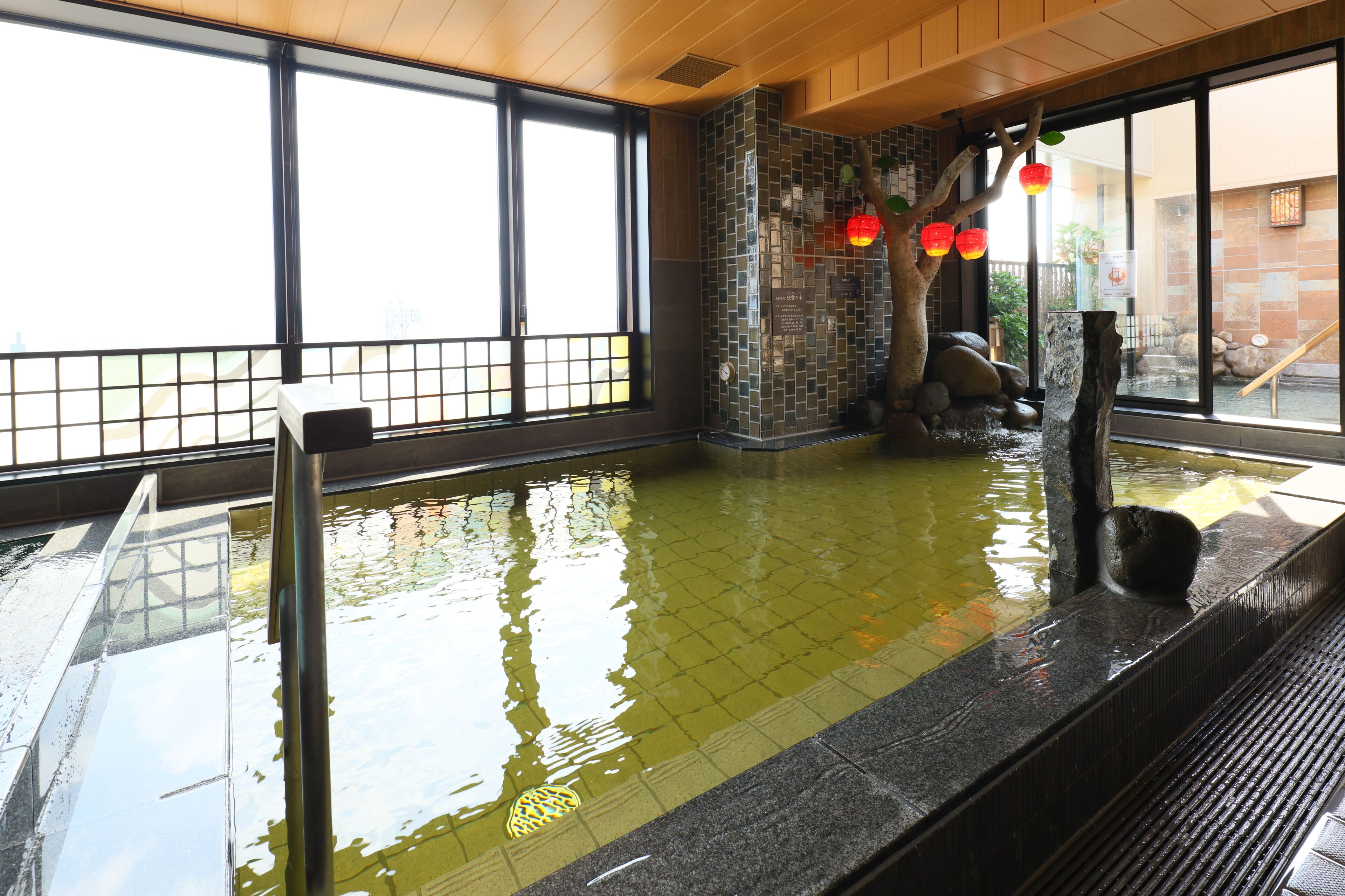 A traditional Japanese onsen with a tiled floor, a wooden bench, and a stone wall.