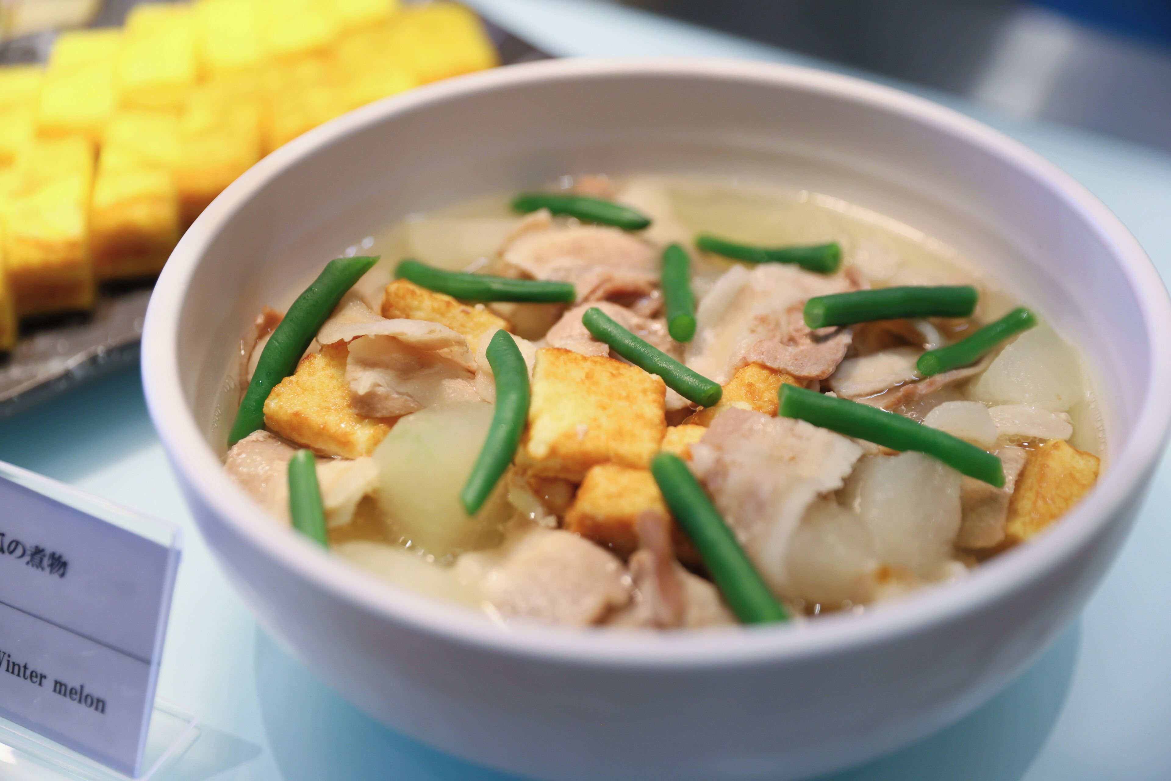 Un bol de soupe contenant du tofu, des haricots verts et de la viande.