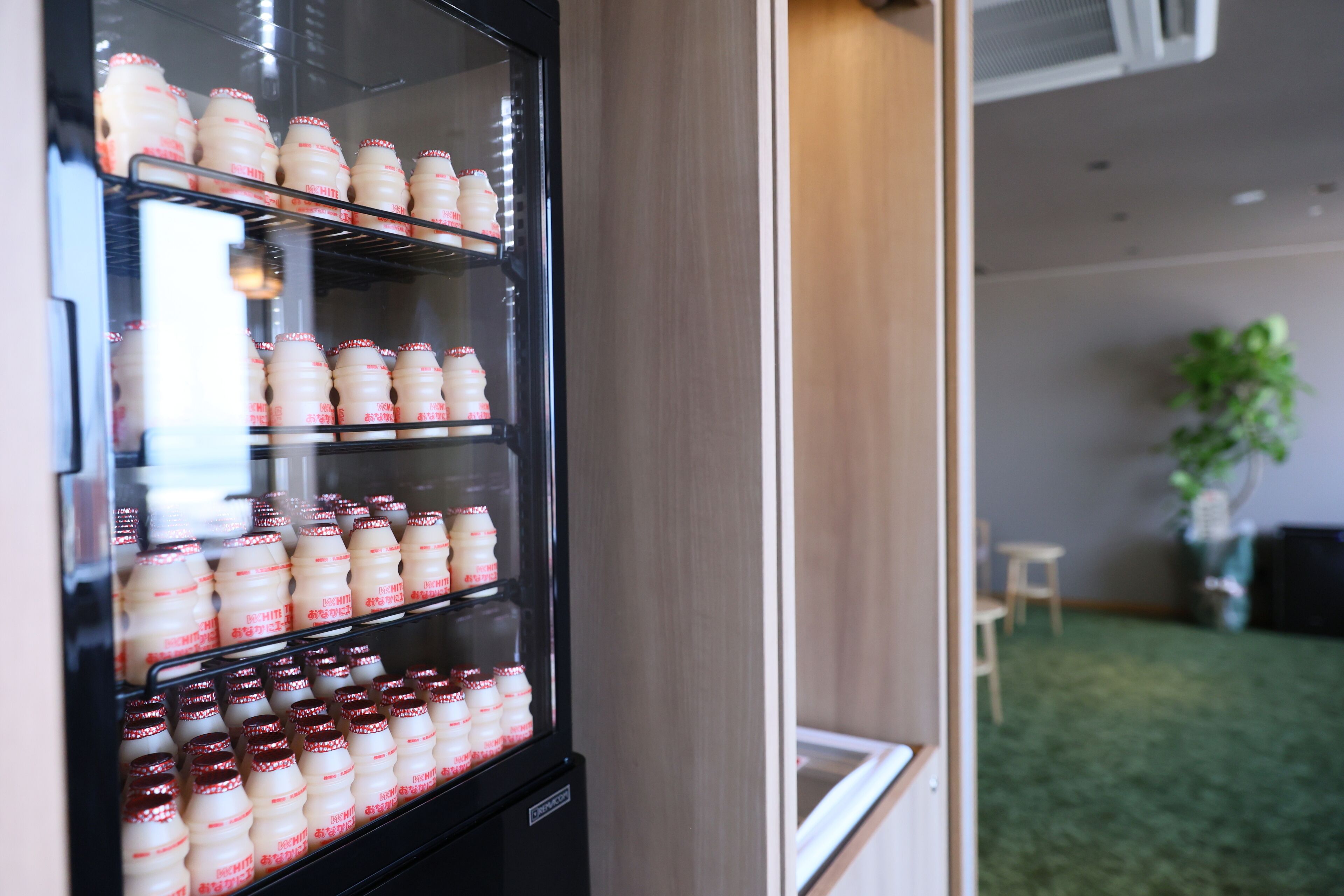 A vending machine stocked with bottles, a wooden wall, and a small table with chairs in the background.