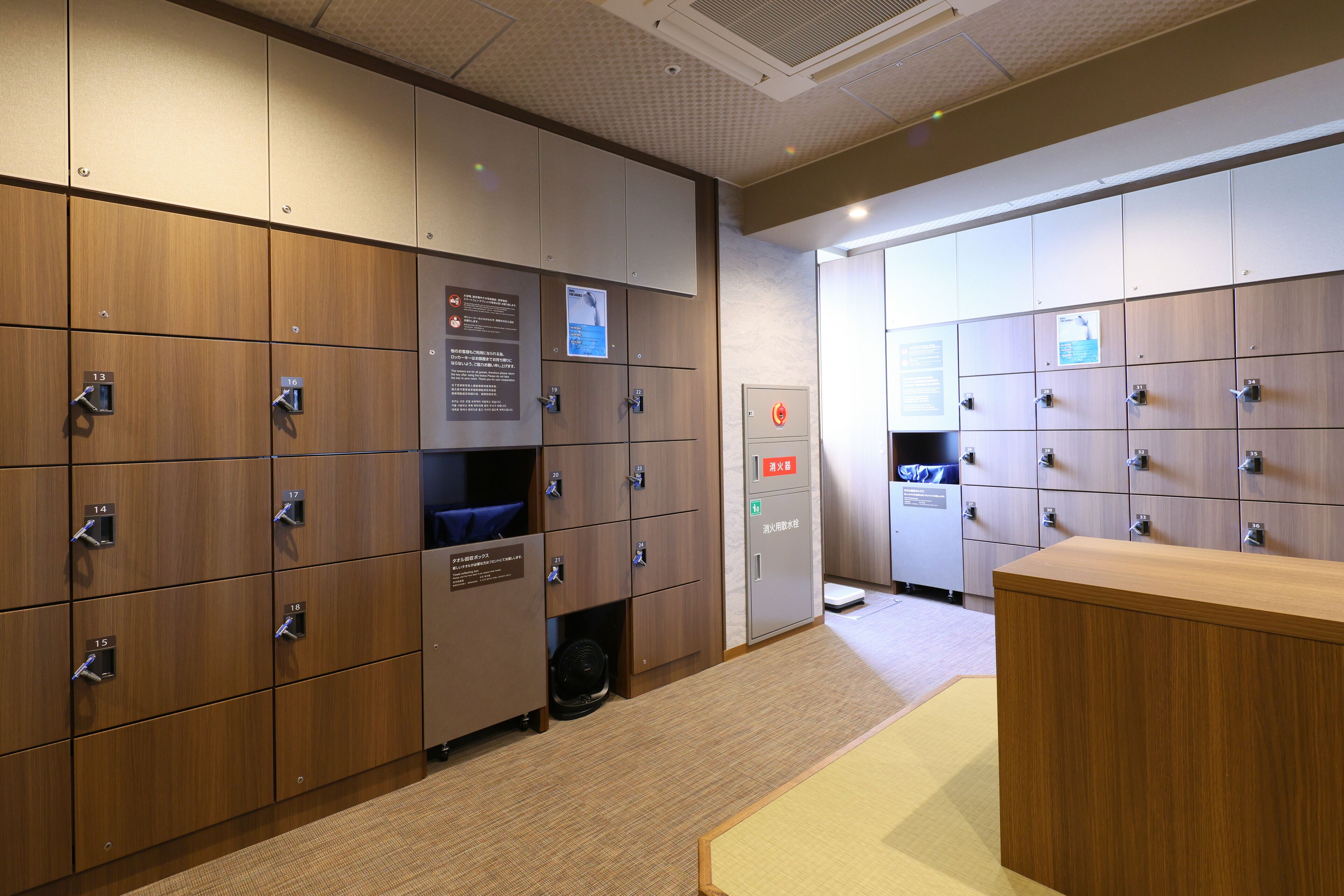 A hotel room with wooden lockers, a reception desk, and a fan.
